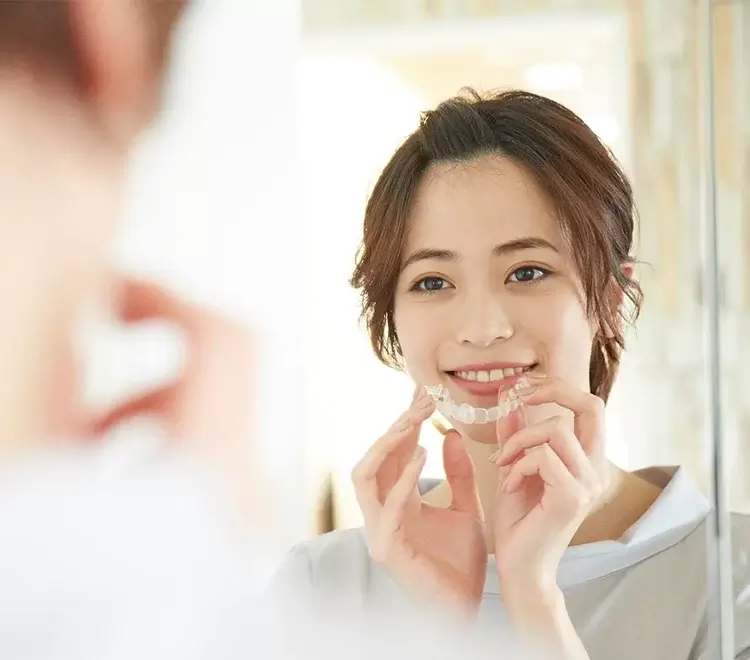マウスピース型矯正装置イメージ（女性がマウスピース型矯正装置を口元に持っていっている）